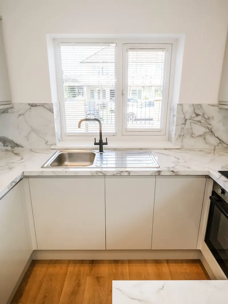New white kitchen (shaker-style), with tiled grey floor and wooden worktops. A wooden kitchen door features in the centre of the picture